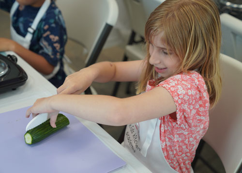 Little girl at Kids Kitchen Academy learning to cut a cucumber